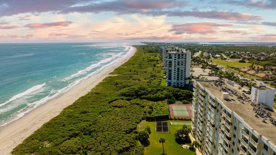 A coastal cityscape with a beach, dense greenery, and high-rise buildings.