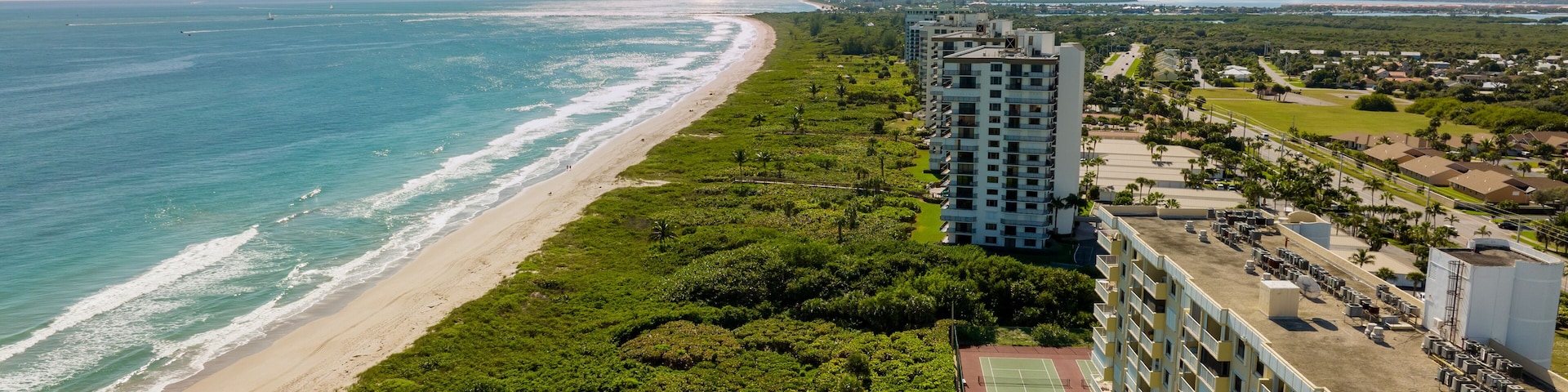 A coastal cityscape with a beach, dense greenery, and high-rise buildings.