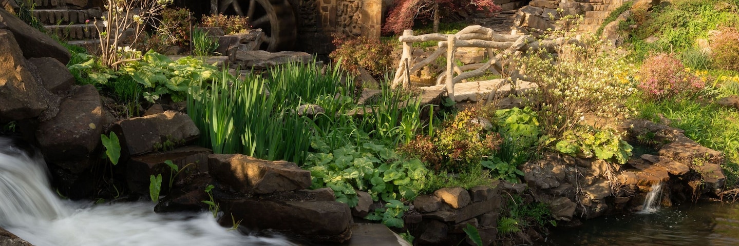 A stone mill house by a flowing stream with surrounding greenery and trees.
