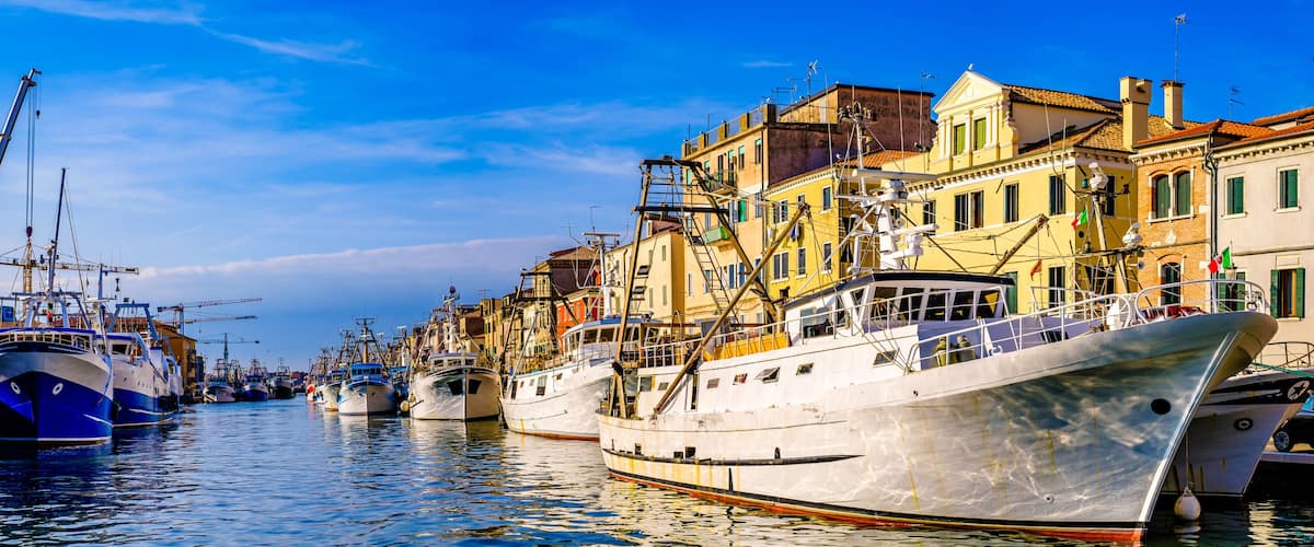 A harbor with multiple boats docked along a waterfront lined with colorful buildings.