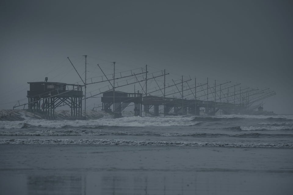 Une jetée côtière dotée de nombreuses structures et de câbles aériens, entourée par les vagues agitées de la mer.