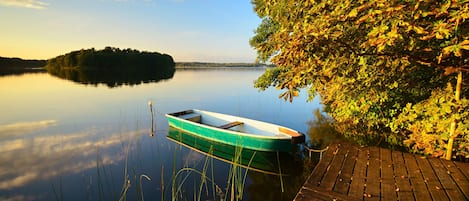 Horse Chestnut Tree by calm lake in full autumn colour at sunset and a rowing boat tied to a wooden pier