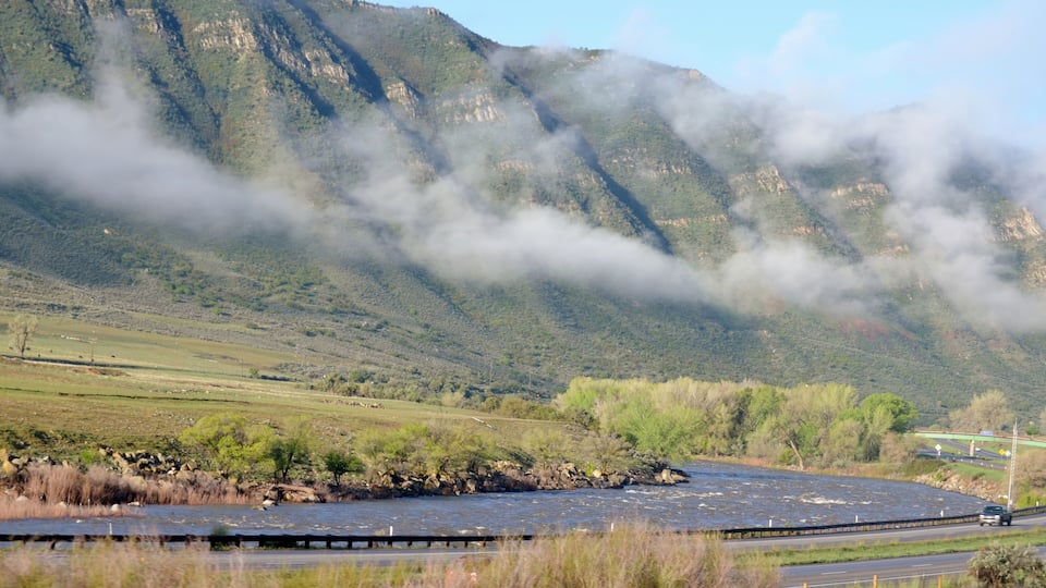 A river flowing through a valley with mountains in the background and a bridge in the foreground.