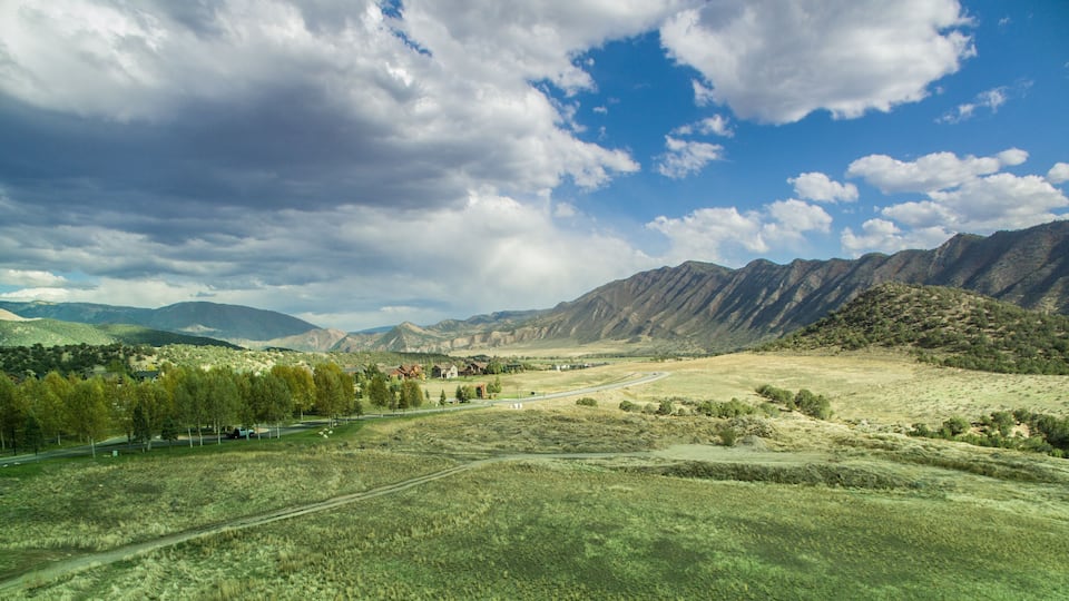 A mountainous landscape with a road, buildings, and trees.