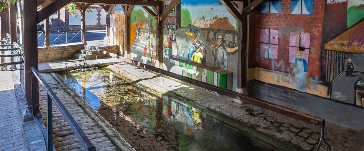 An indoor space with a wooden ceiling, a reflective water feature, and colorful graffiti on the walls.