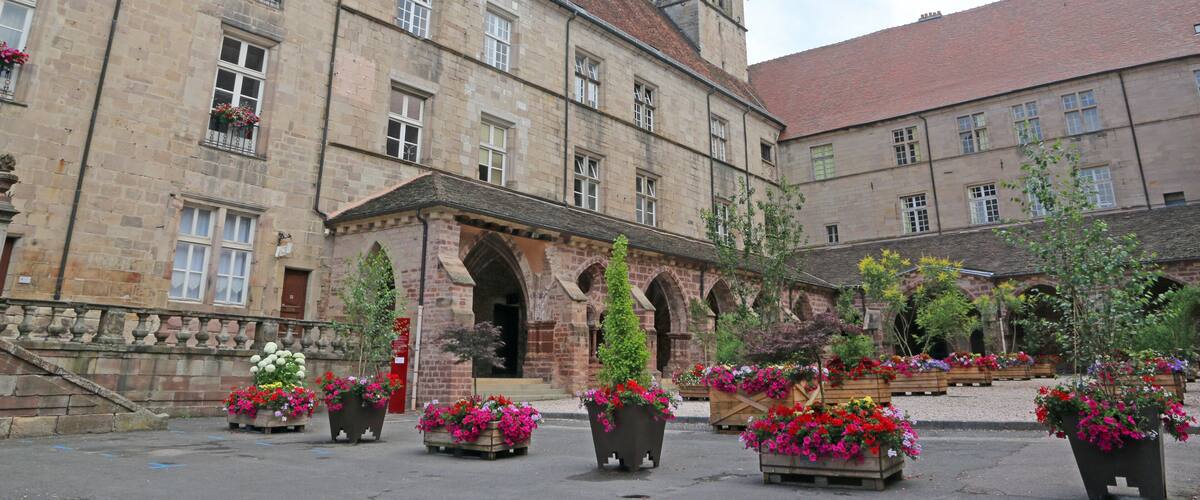 A historic building with a clock tower, flower beds, and arched walkways.