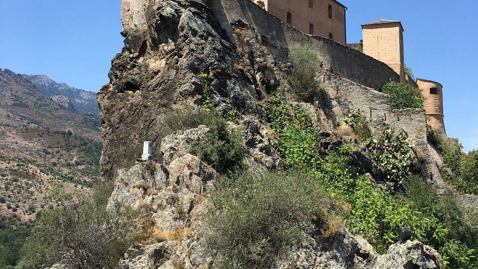 A historic stone castle perched on a rocky cliff with a paved walkway in the foreground.