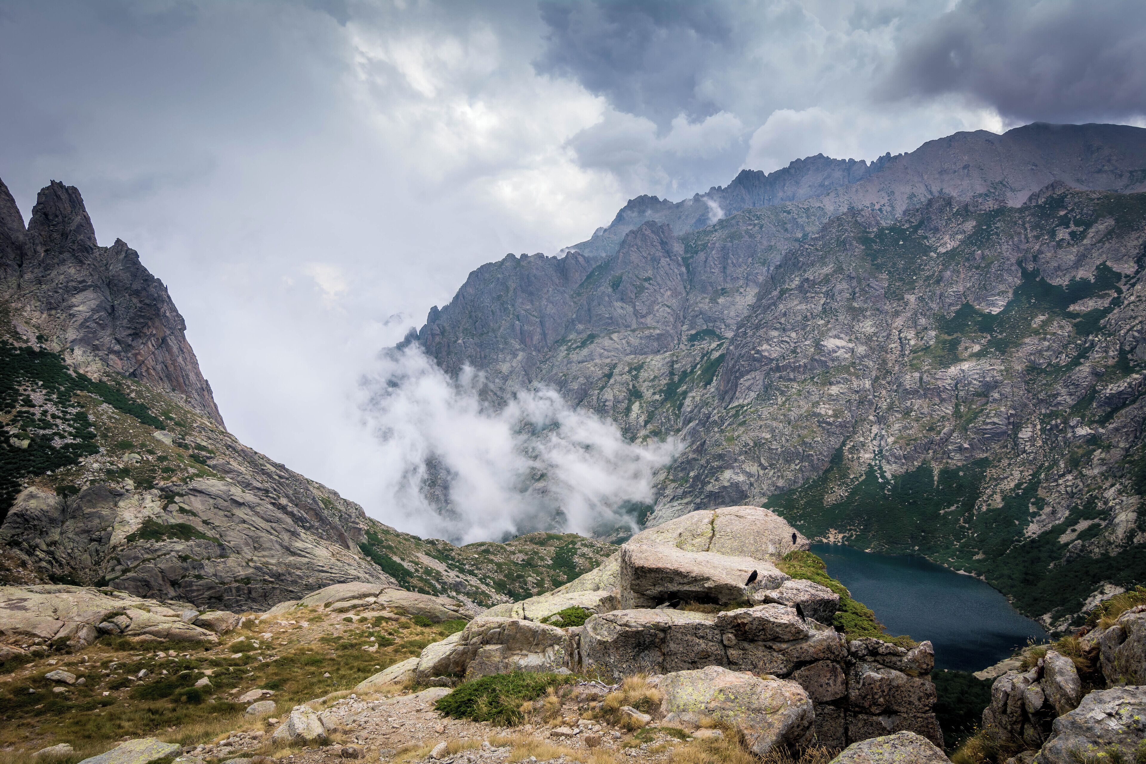 A mountainous landscape with a lake, rocky terrain, and clouds.