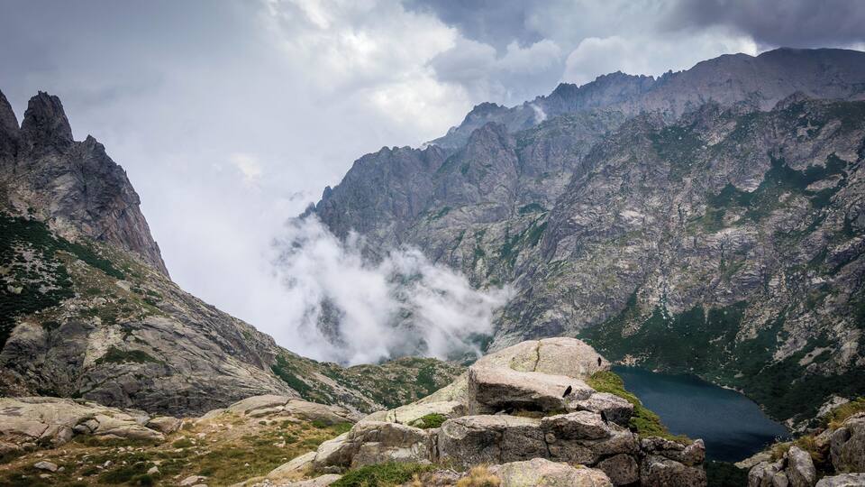 A mountainous landscape with a lake, rocky terrain, and clouds.