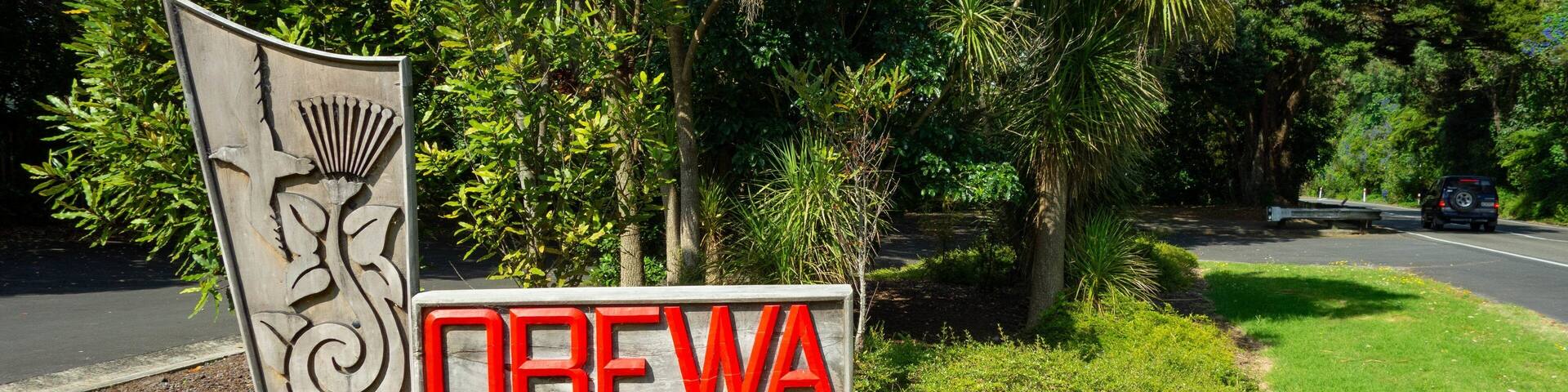 A sign with the word "OPEWA" in red letters, surrounded by greenery and trees.