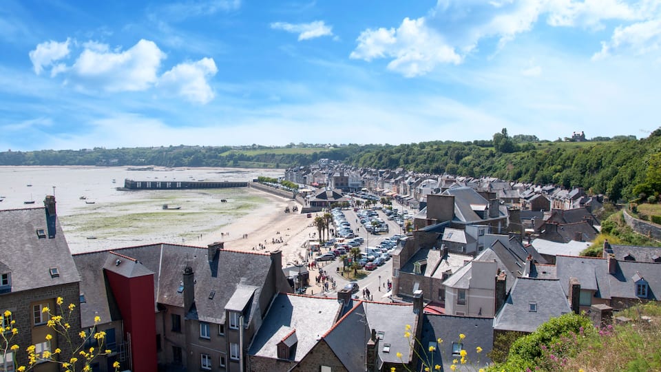 A coastal town with a beach, parked cars, and buildings.