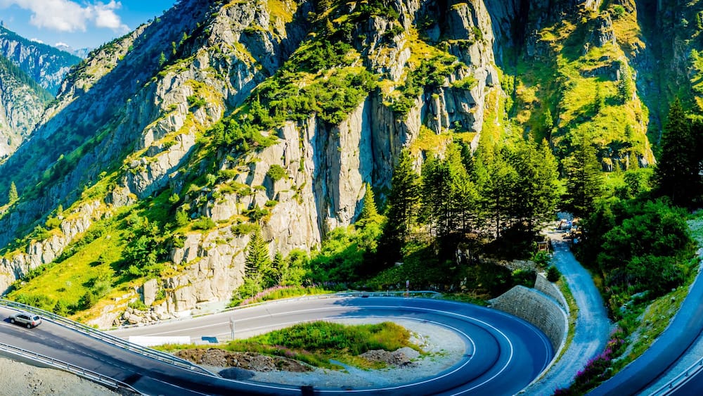 Eine kurvenreiche Bergstraße mit Schutzrail, umgeben von steilen Klippen und üppiger Vegetation.