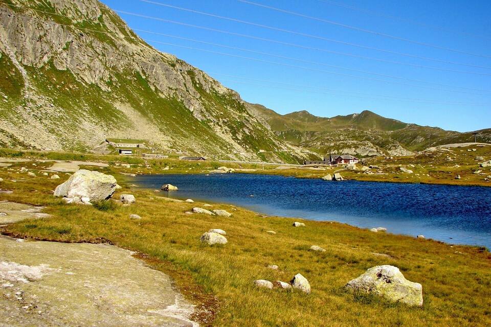 A lake surrounded by mountains, with a few buildings and rocks in the foreground.