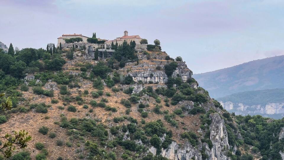 A historic building complex on a hillside with surrounding rocky terrain and sparse vegetation.