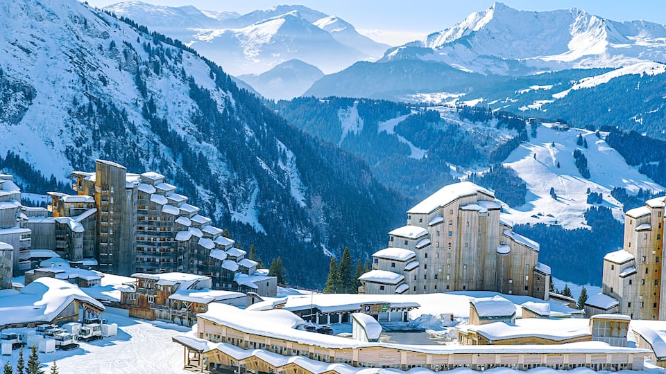 A snow-covered mountain resort with ski slopes, buildings, and a clear sky.
