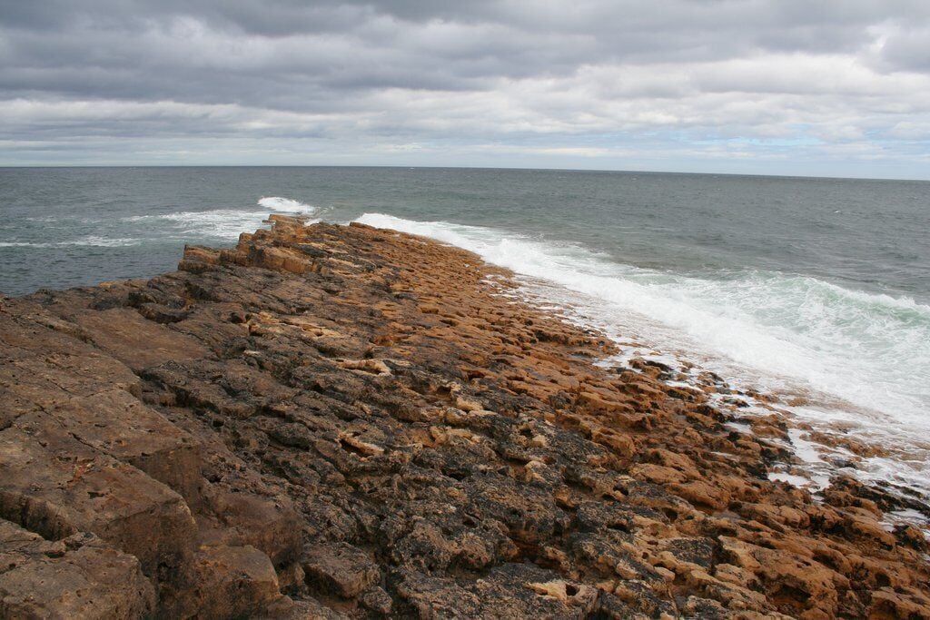 Litoral rochoso com ondas quebrando na costa sob um céu nublado.