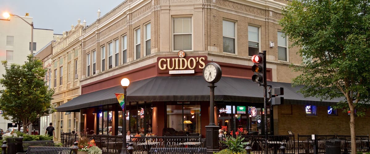 A historic building with a 'GUIDO'S' sign, outdoor seating, and a clock.