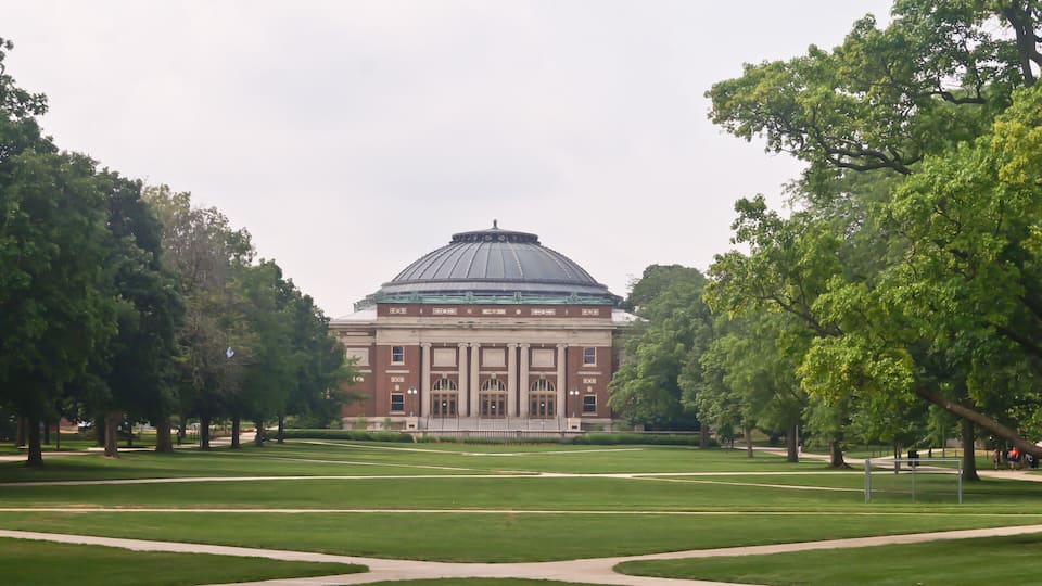 A large building with a dome roof surrounded by a well-maintained lawn and trees.
