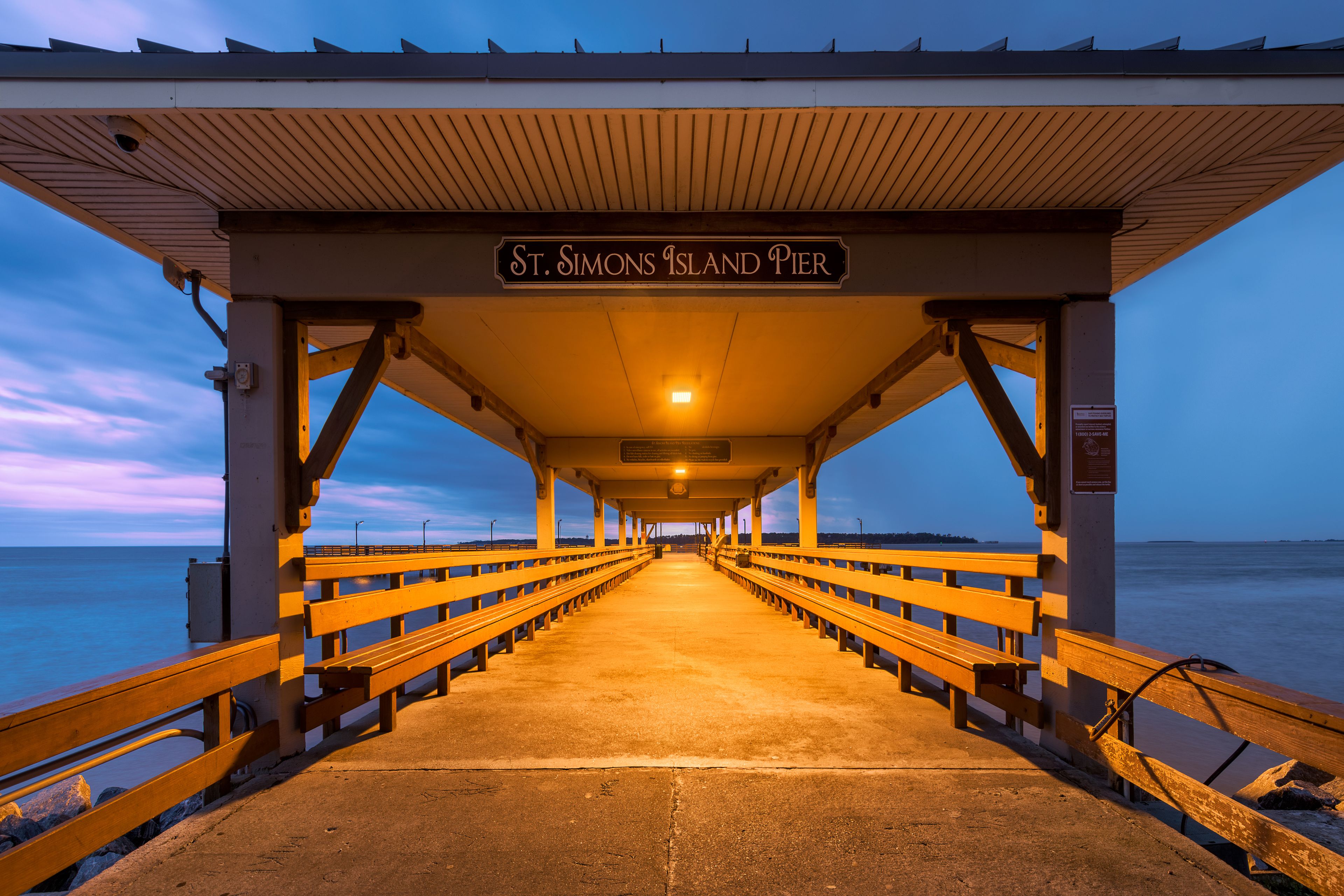 A pier at St. Simons Island Pier with wooden railings and a sign.