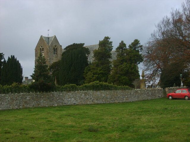 A stone church with a pointed roof and a stone wall in the foreground.