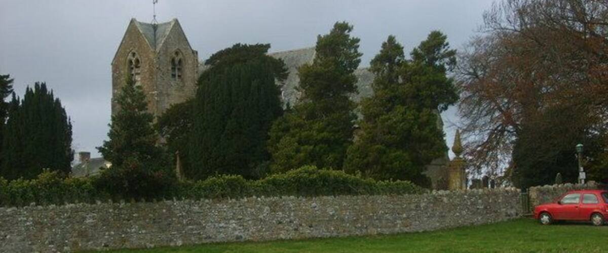 A stone church with a pointed roof and a stone wall in the foreground.