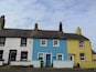 A row of three houses painted in white, blue, and yellow, with a blue door and a green trash bin in front.