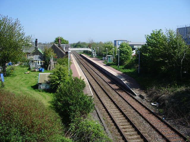 A railway track with a bridge in the background, surrounded by greenery and a small building.