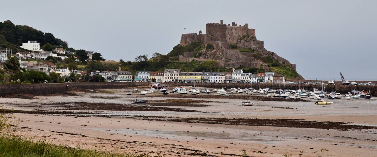 A coastal town with a prominent castle on a hill, a marina with boats, and residential buildings along the shore.