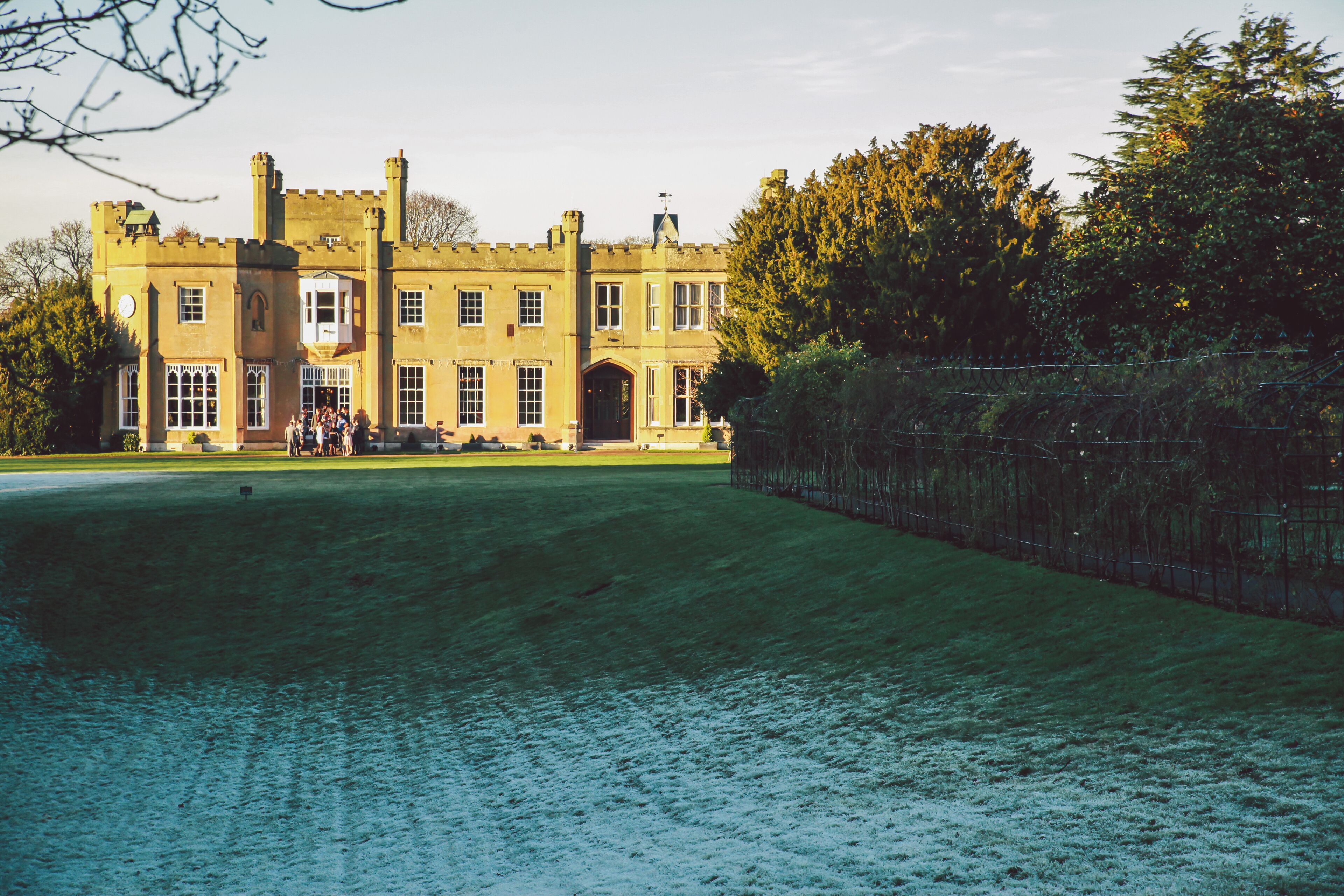 A large, historic building with a symmetrical facade, a central entrance, and a surrounding lawn.