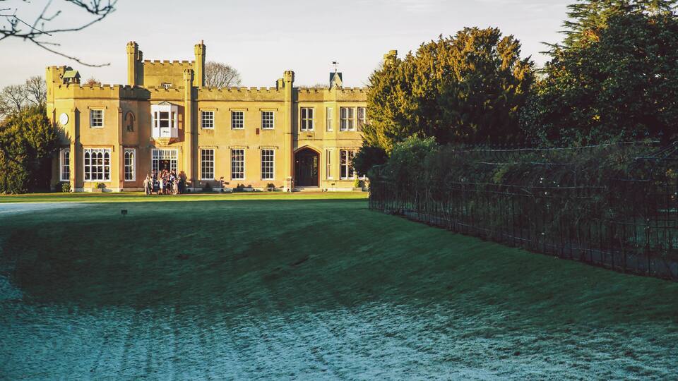 A large, historic building with a symmetrical facade, a central entrance, and a surrounding lawn.