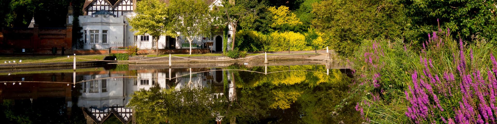 A tranquil riverside scene with a historic building, lush greenery, and a clear blue sky.