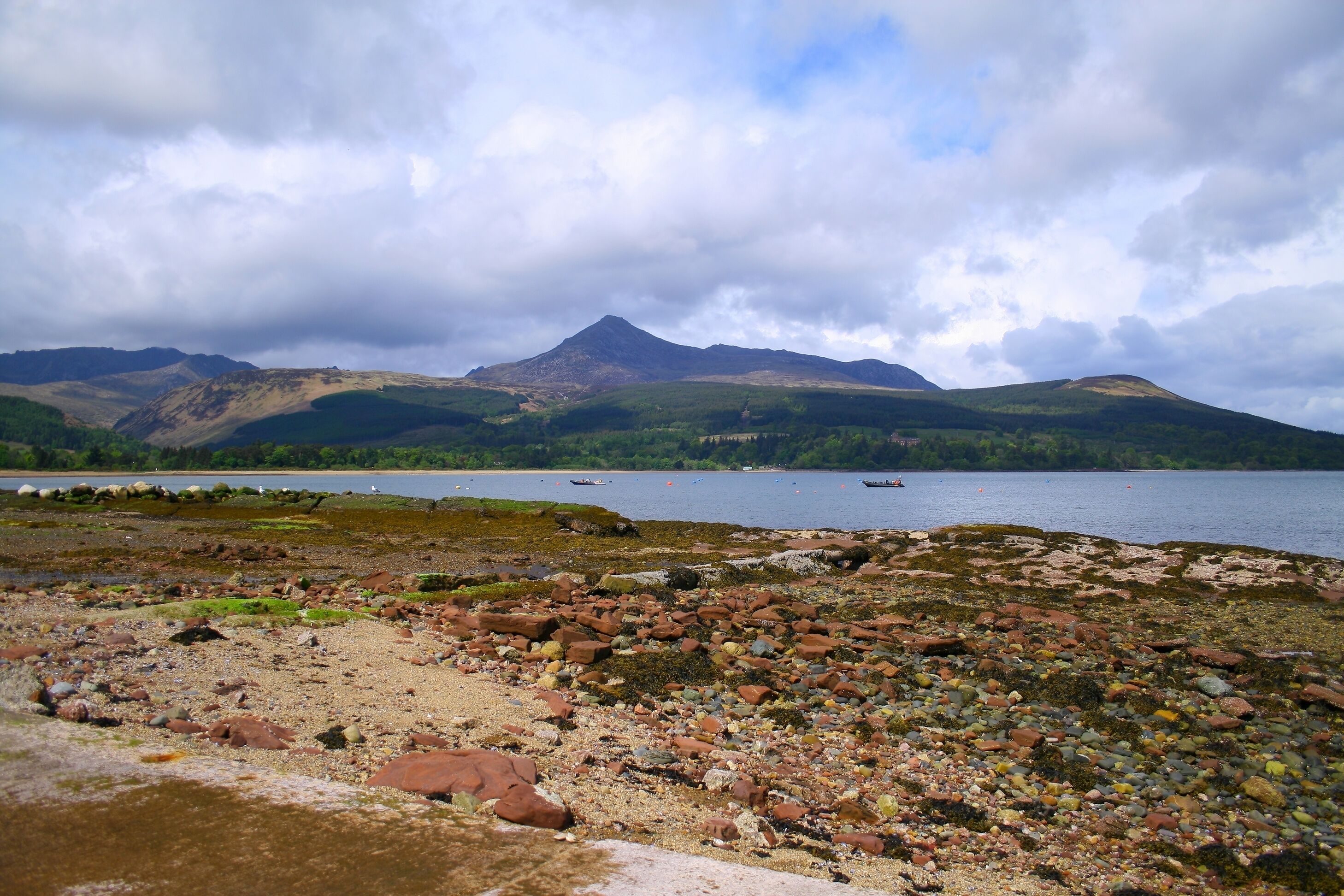 A rocky shoreline with a lake and mountains in the background.