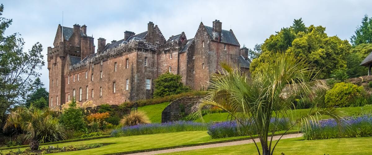 A historic castle with a well-manicured garden and a large palm tree.