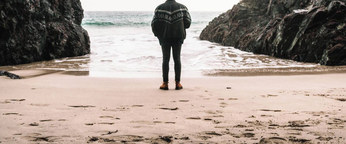 A person standing on a sandy beach between rocky formations, looking out at the ocean.