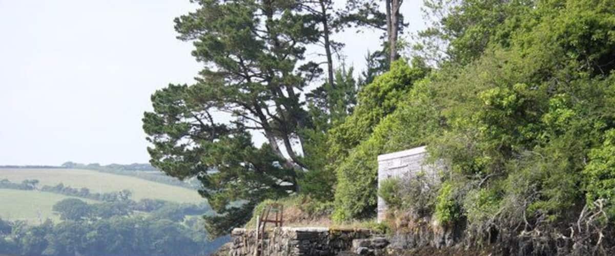 Un paisaje costero con un muro de piedra, un edificio blanco y un árbol grande.