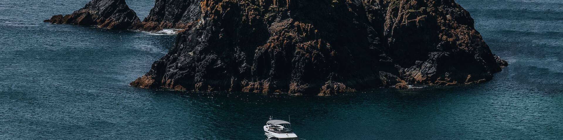 View of the craggy rock formation at Kynance Cove with a small motorboat floating on the deep blue sea in Helston, England, United Kingdom.