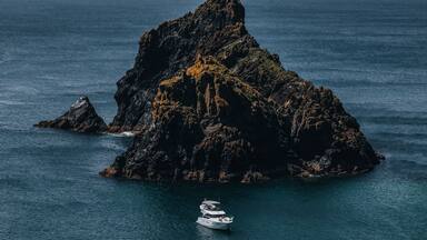 A rocky island surrounded by calm sea with a boat near the shore.
