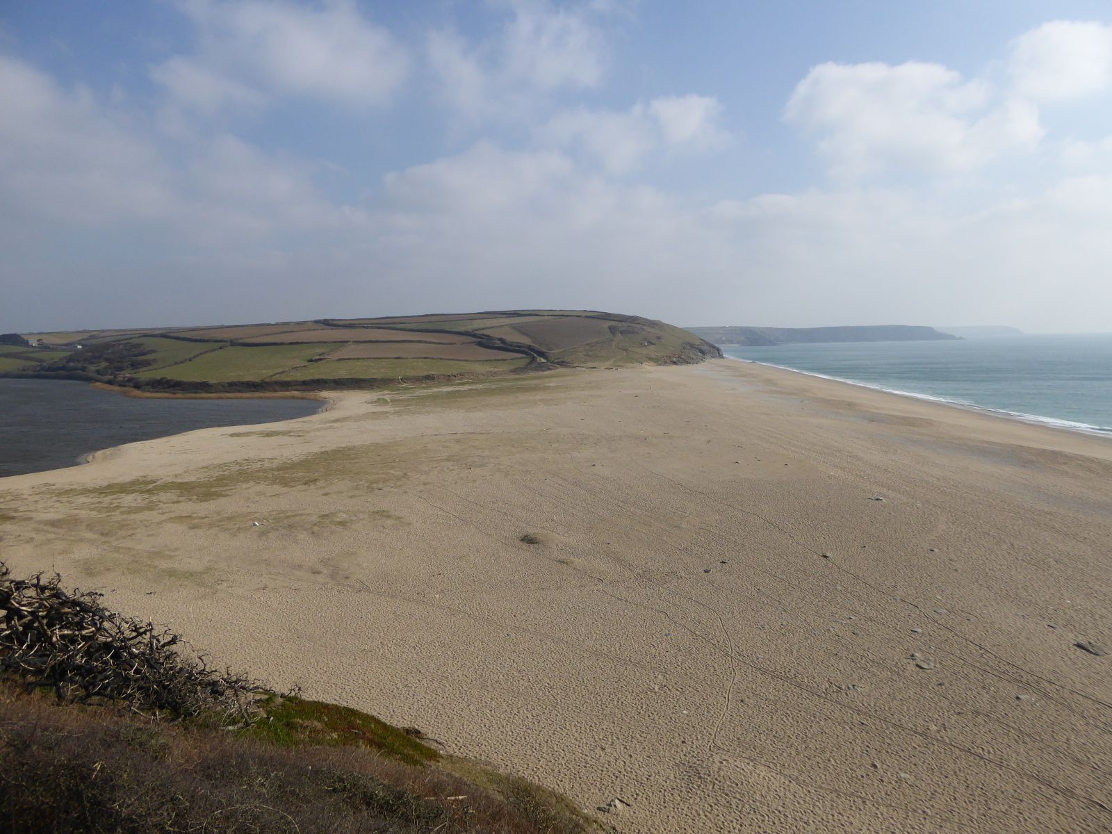 A coastal landscape with a sandy beach, rolling hills, and a body of water.