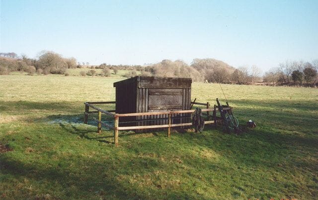 A wooden structure in a grassy field with a fence and a bicycle.