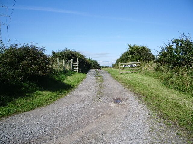 A gravel road with a wooden gate and a signpost in a rural setting.