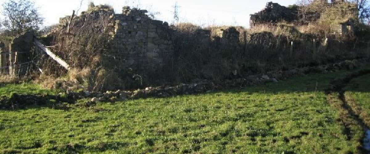 A grassy field with ancient stone ruins and a small structure in the background.