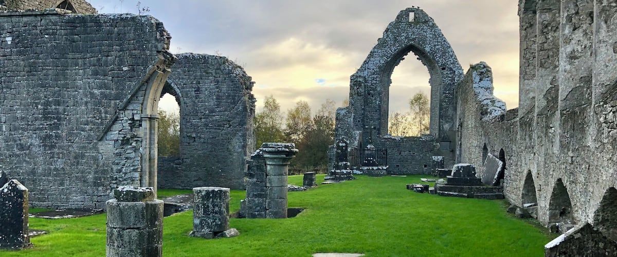 The ruins of an old stone structure with arched doorways and a grassy courtyard.