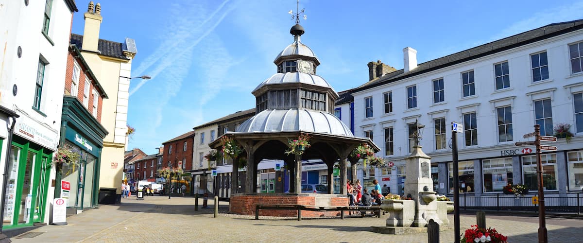 A cobblestone square with a gazebo, flower pots, and historic buildings.
