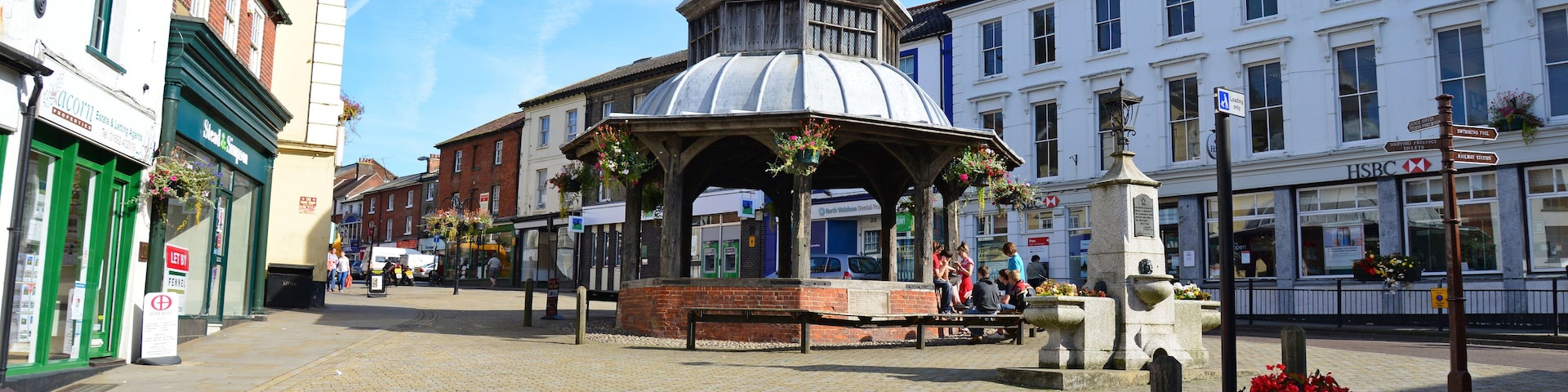 A cobblestone square with a gazebo, flower pots, and historic buildings.