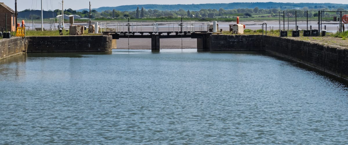 A canal lock with a bridge, water, and industrial structures in the background.