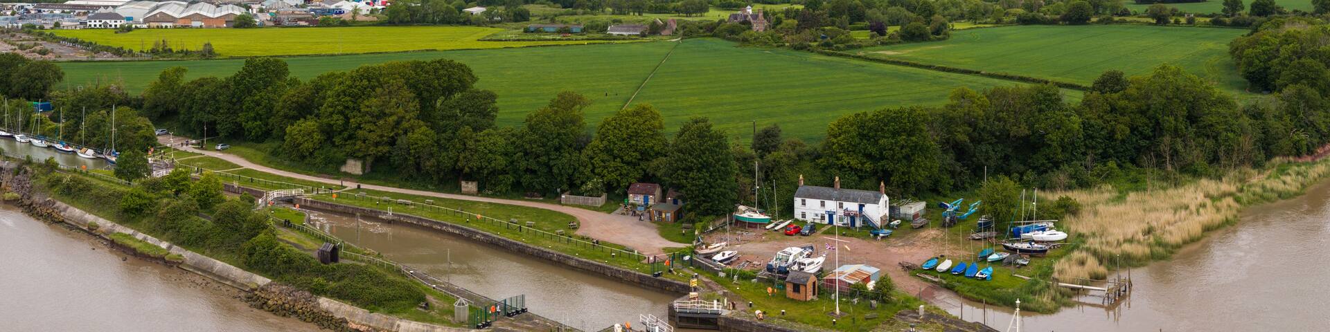 A riverside town with a lock system, boats, and surrounding green fields.