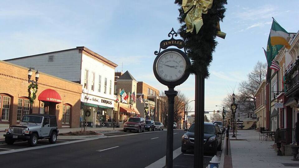 A street with shops, a clock, and a decorated post.