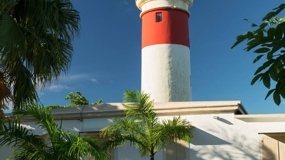 A lighthouse with a red and white tower, surrounded by palm trees and a clear blue sky.