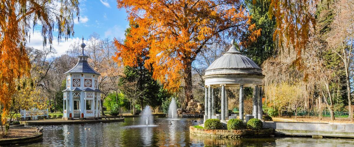 A tranquil park with a pond, a gazebo, and a pavilion with a fountain.