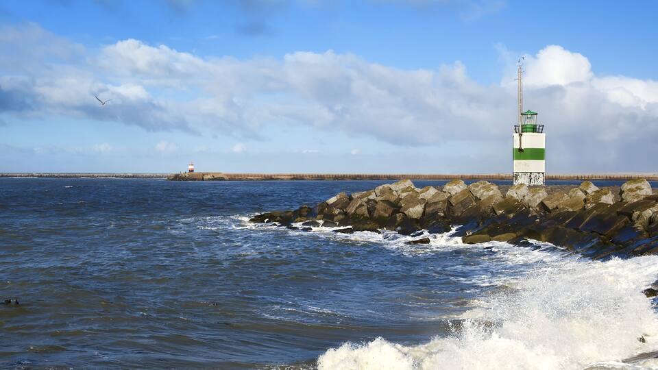A lighthouse on a rocky breakwater with waves crashing against it.